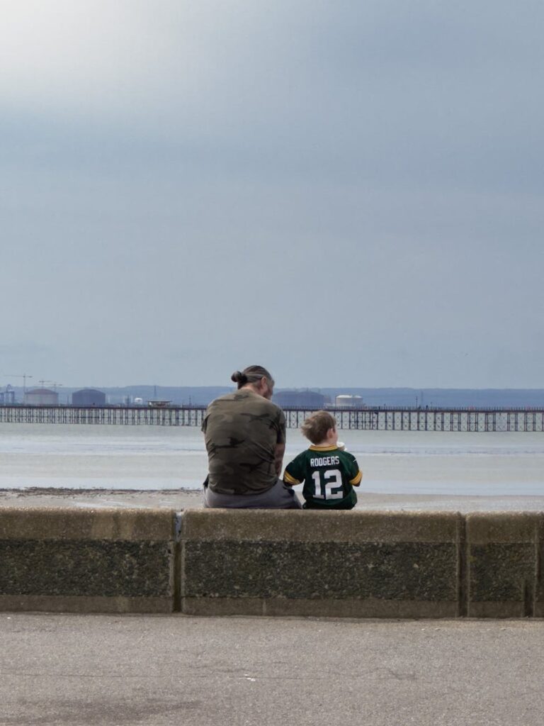 back view of a man and little boy sitting near a body of water